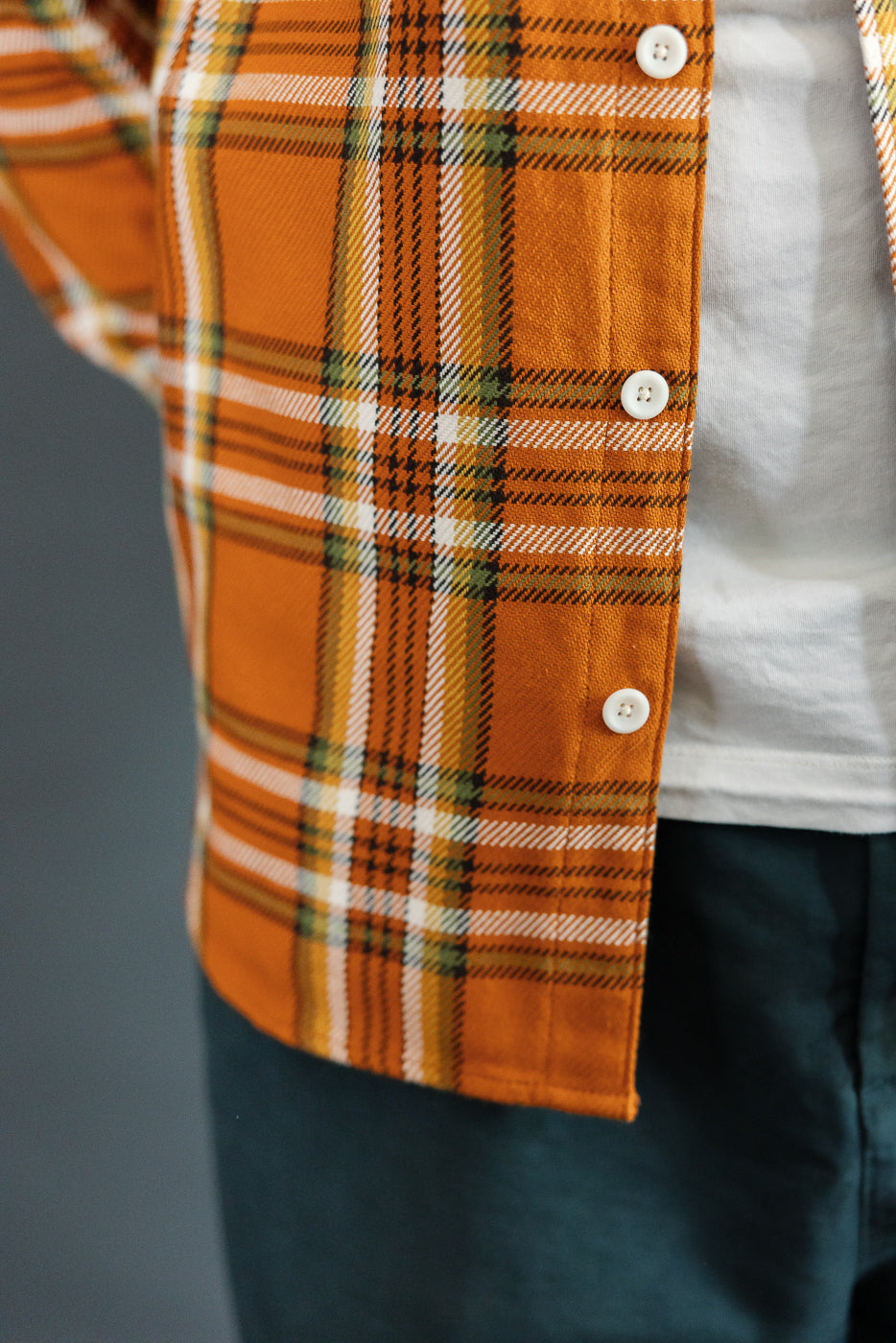 Close-up front view of male model wearing orange plaid flannel shirt with white buttons, athletic build