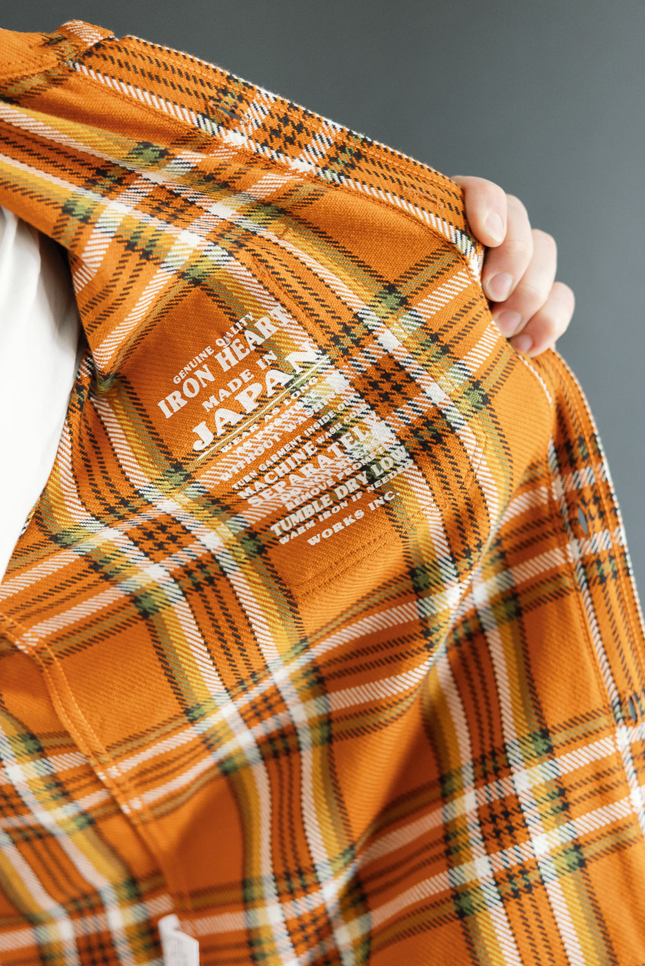 Close-up of orange plaid shirt front, showcasing tag details and fabric texture.