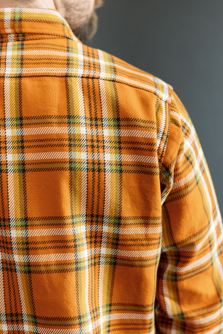 Close-up back view of male model in orange plaid shirt, showcasing fabric texture and collar detail.