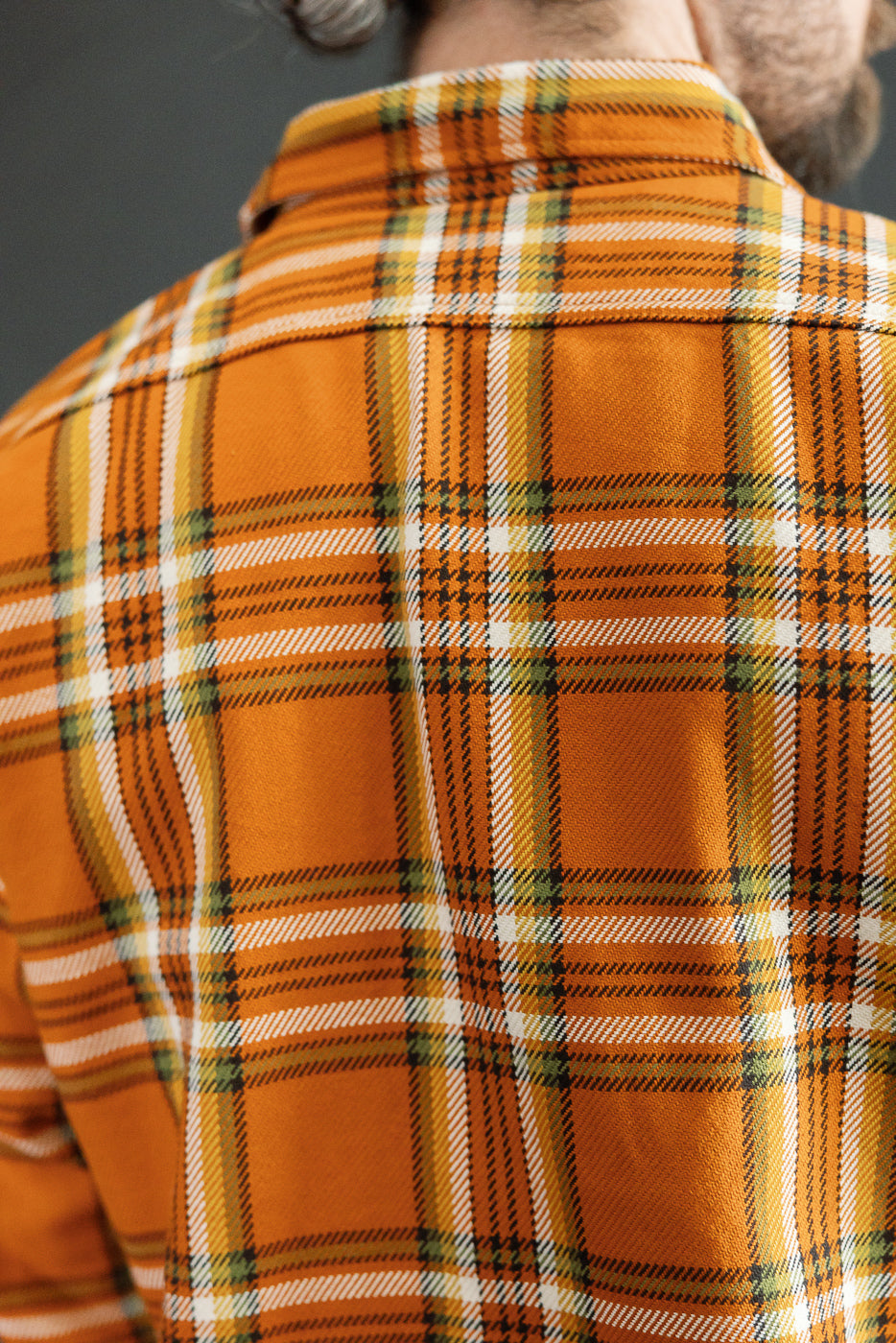 Back view of male model in orange plaid shirt, showcasing collar and fabric texture, athletic build.