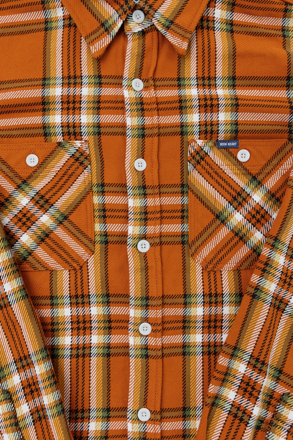 Close-up front view of orange plaid shirt with white buttons, chest pockets, and Iron Heart tag.