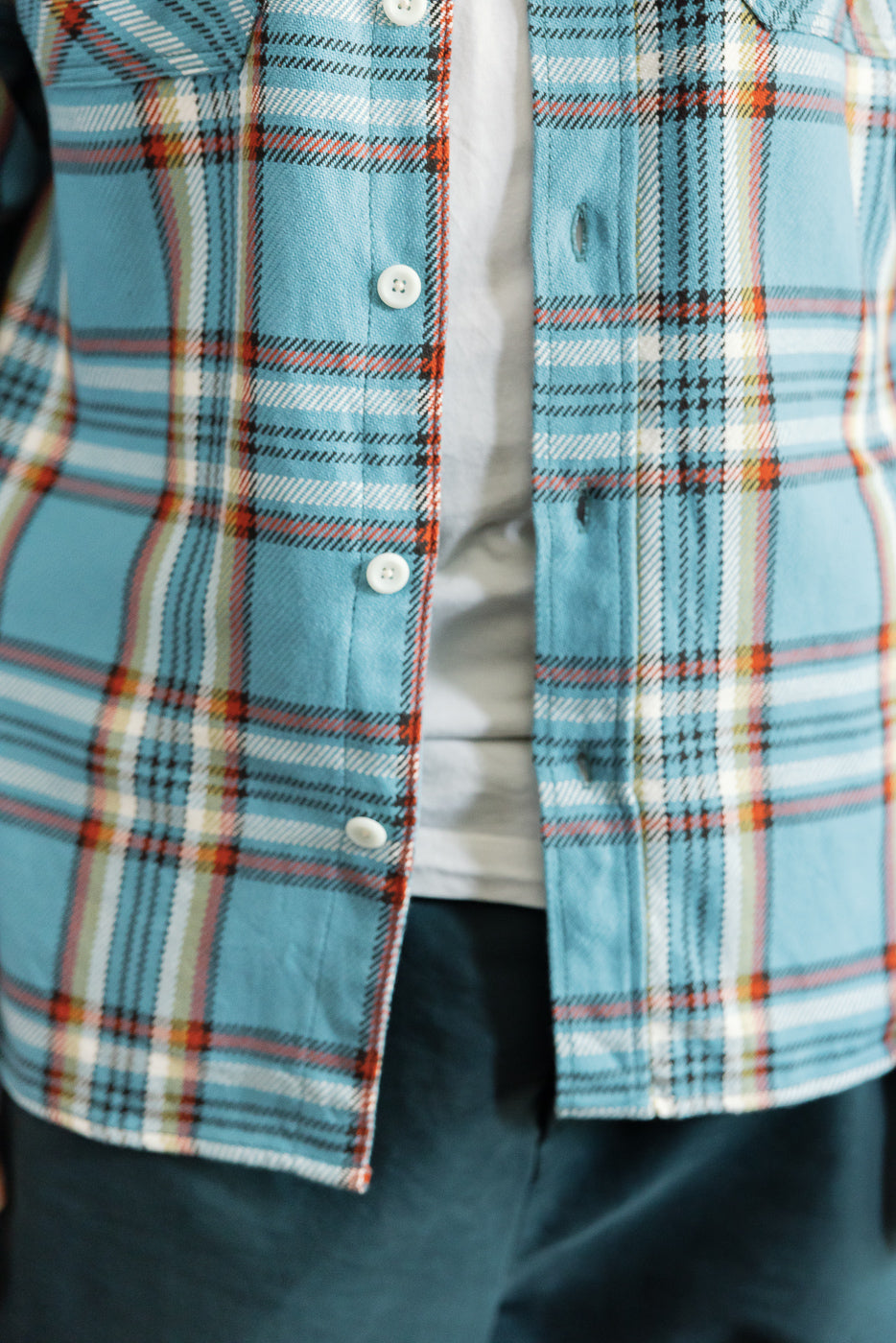 Close-up front view of male model's plaid shirt with white buttons, blue base, and orange accents