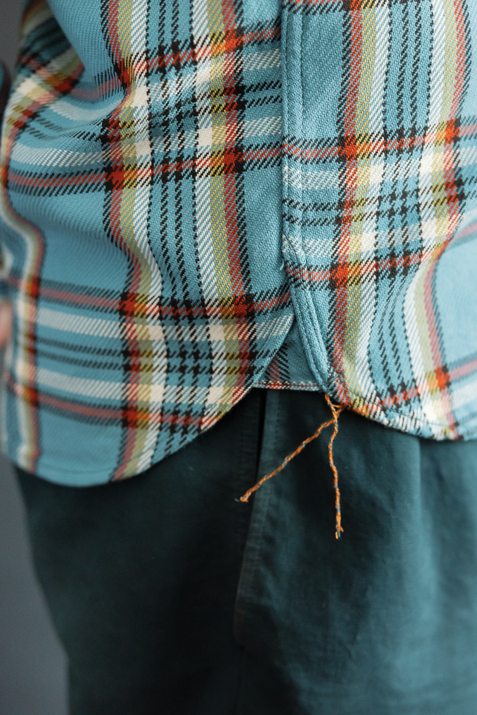 Close-up of male model's back, showing plaid shirt hem with orange thread detail, athletic build.