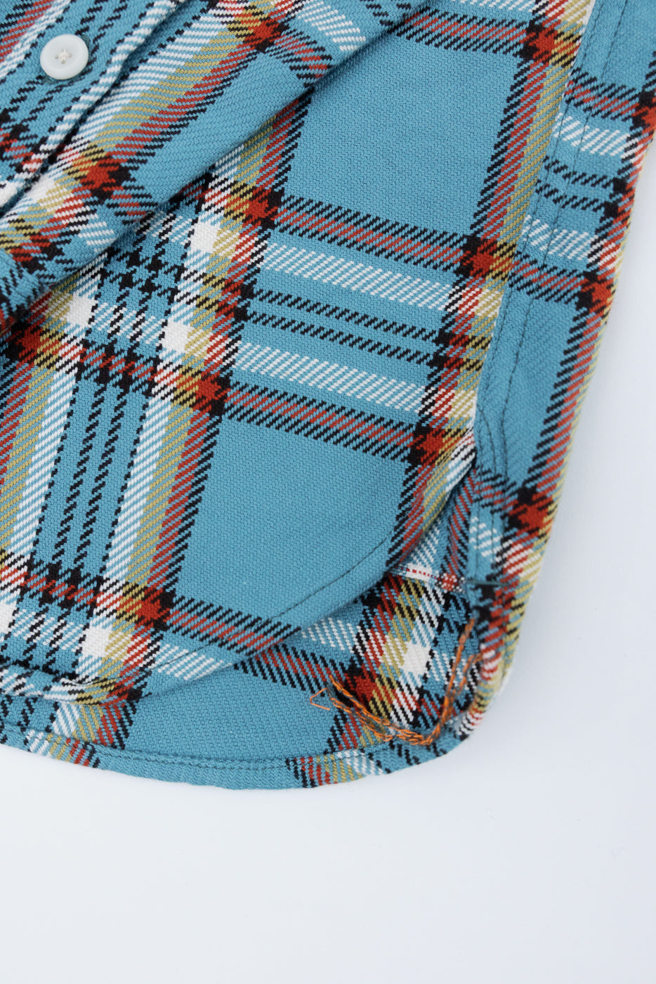 Close-up of blue plaid shirt front, showcasing button, fabric texture, and hem detail
