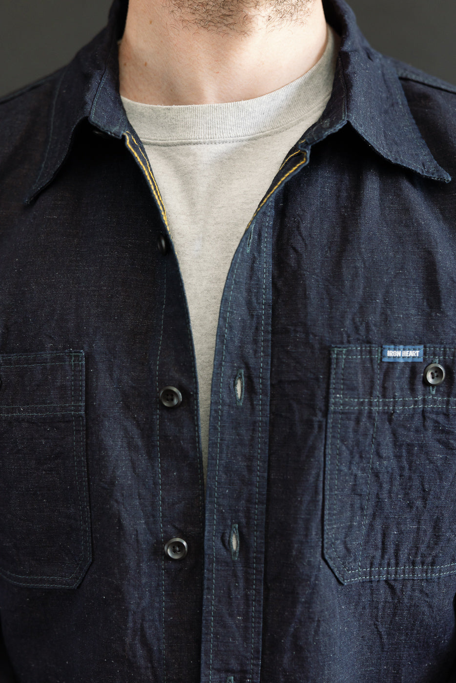 Close-up front view of indigo cotton-linen chambray work shirt on male model, showing collar, chest pockets, and textured fabric detail. Model is 5'9