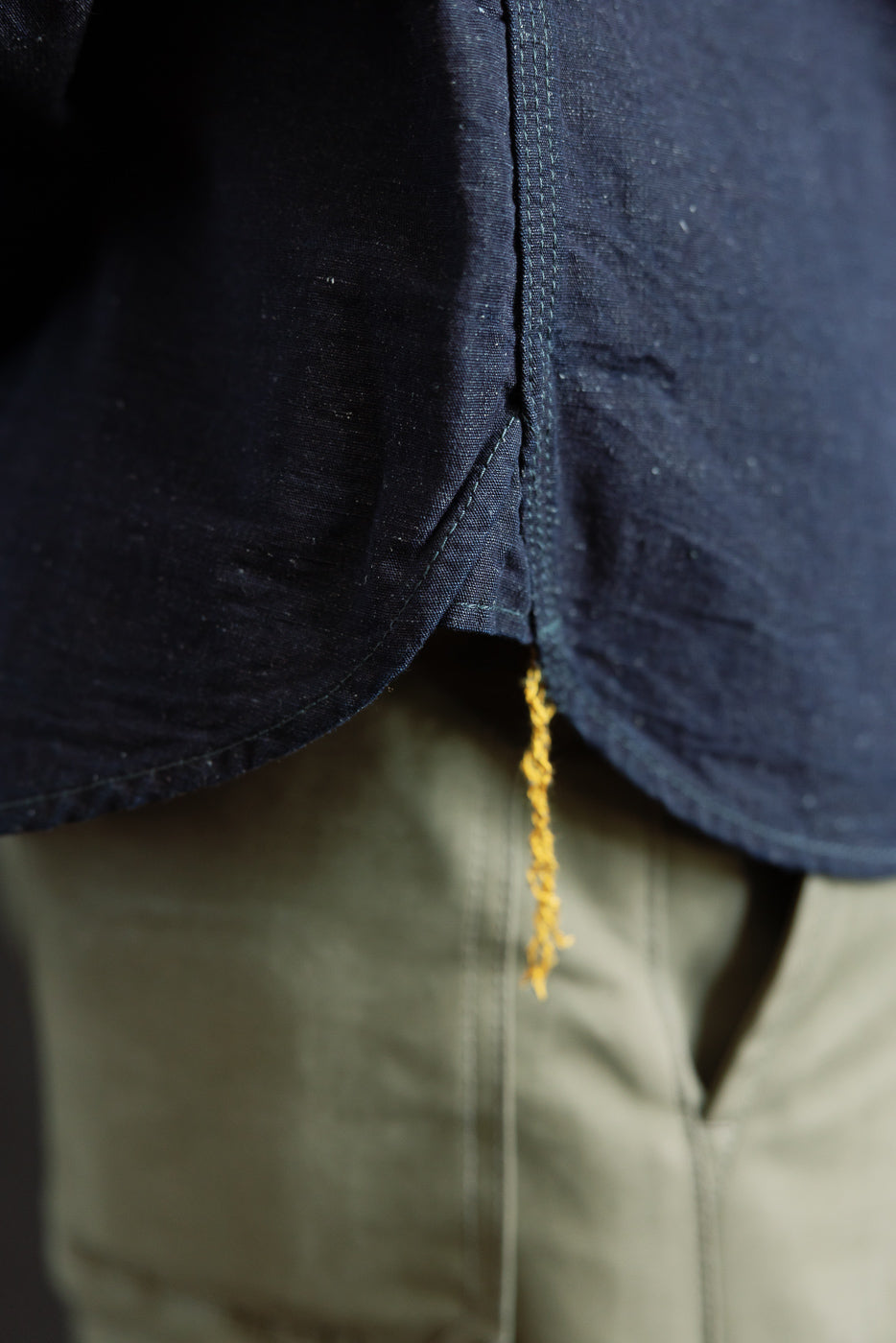 Close-up of male model wearing indigo chambray work shirt, showing side hem and shirt texture.