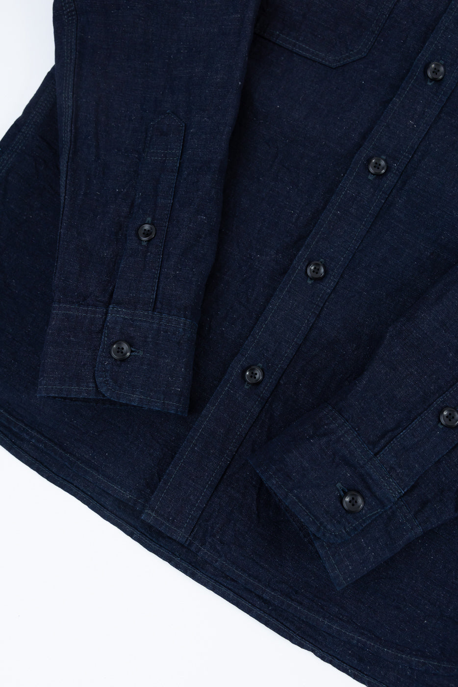 Close-up of front lower section of indigo chambray work shirt showing sleeve cuffs, buttons, and fabric texture.