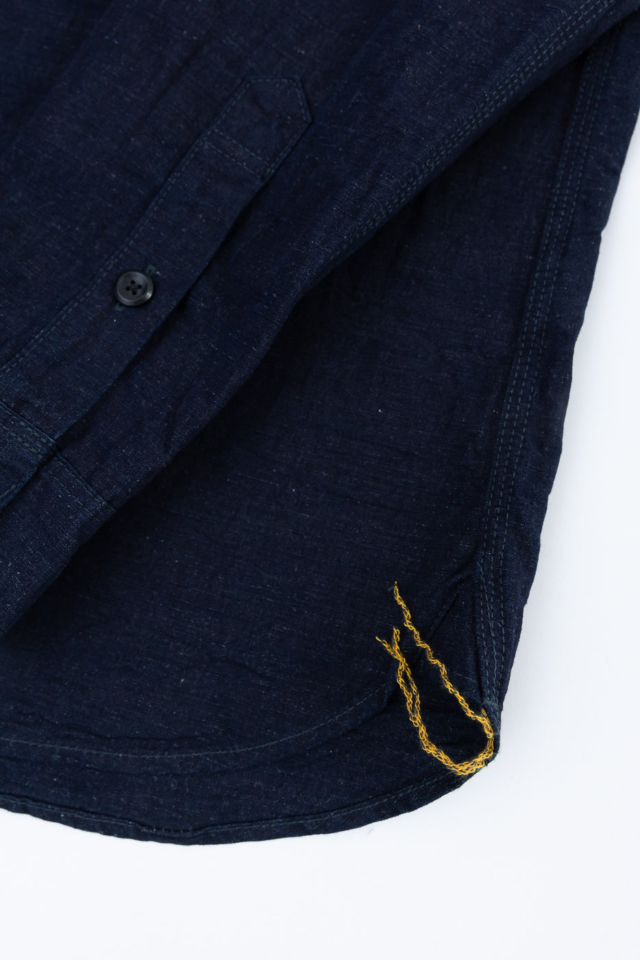 Close-up of indigo cotton linen chambray work shirt hem, front side, showing button and stitching detail.