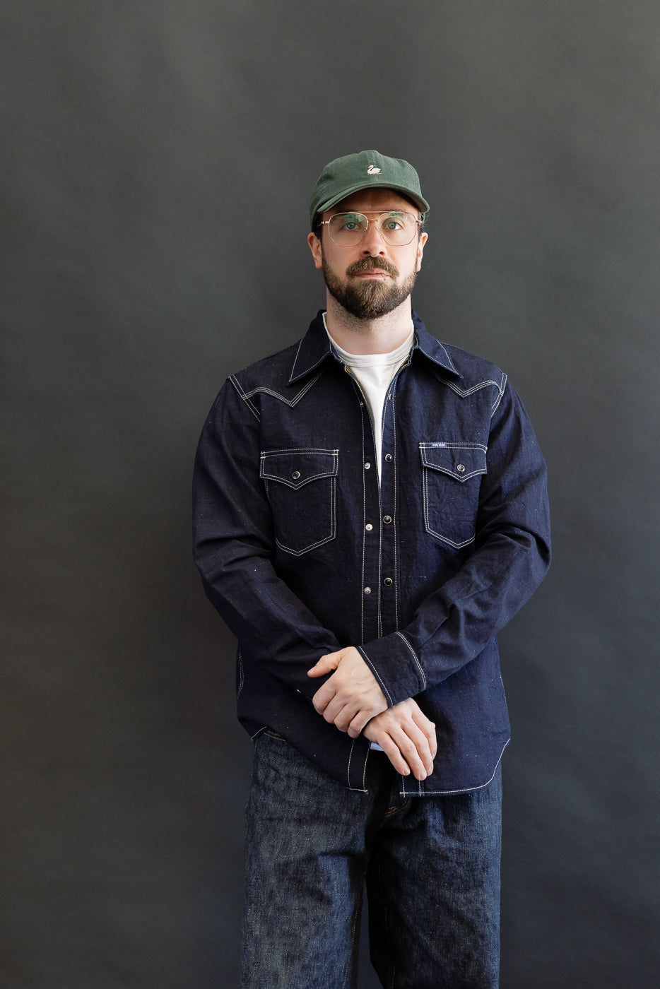 IHSH-444-IND - 7oz Cotton Linen Chambray Western Shirt - Indigo, worn by a man with a green cap and glasses, featuring snap fastenings and contrast stitching, styled over a white T-shirt.