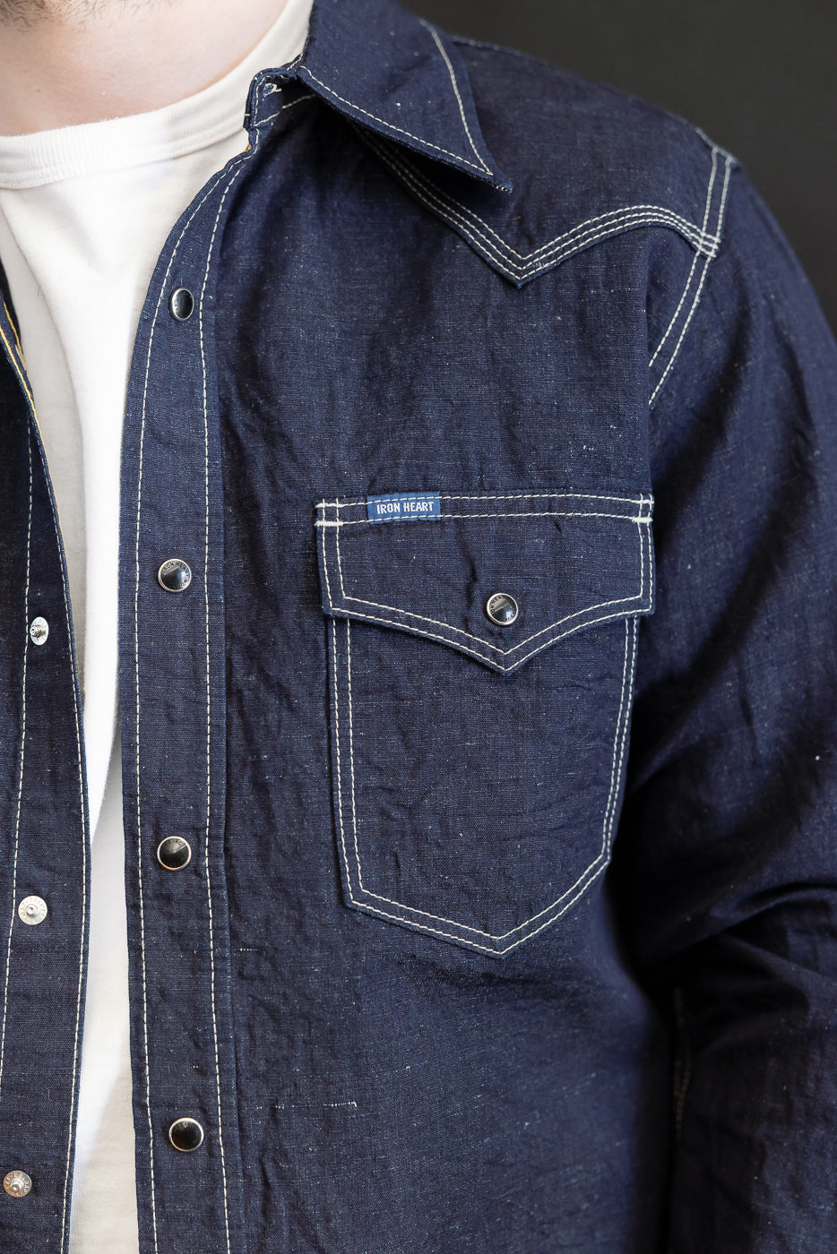 Close-up of the IHSH-444-IND - 7oz Cotton Linen Chambray Western Shirt in dark indigo, showcasing snap-button closure, contrast white stitching, and a western-style flap chest pocket with Iron Heart label.