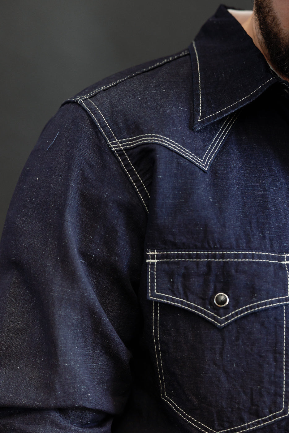 Close-up of the IHSH-444-IND - 7oz Cotton Linen Chambray Western Shirt in dark indigo, featuring a pointed collar, white topstitching, and a flap chest pocket with a metal snap.