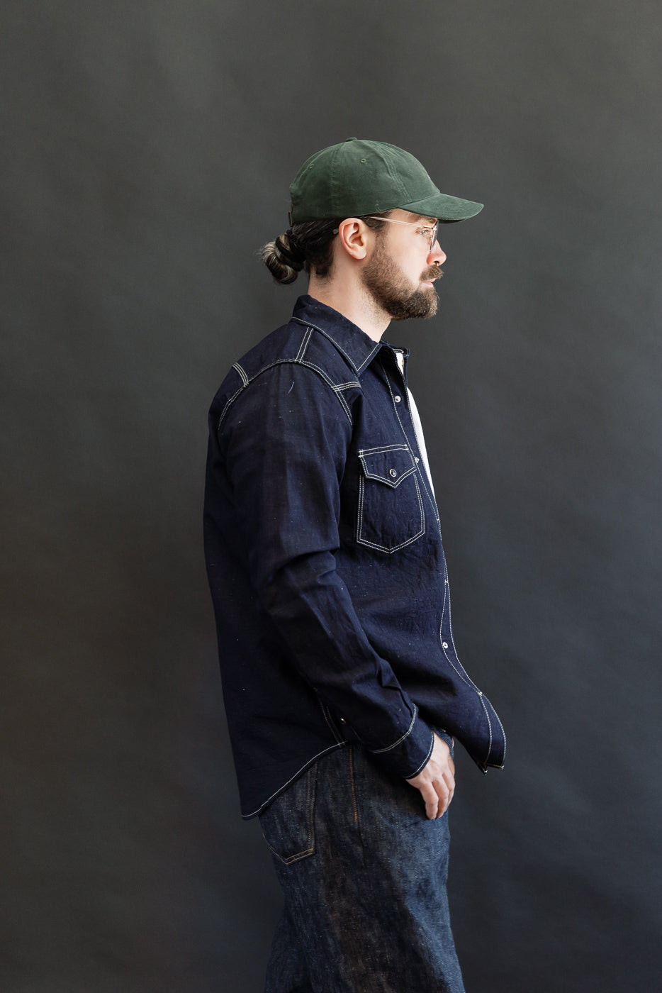 Man models IHSH-444-IND - 7oz Cotton Linen Chambray Western Shirt, showcasing its Western-style yokes, contrast stitching, and snap fastenings, paired with blue jeans, embodying Dant's rugged, heritage-inspired style.