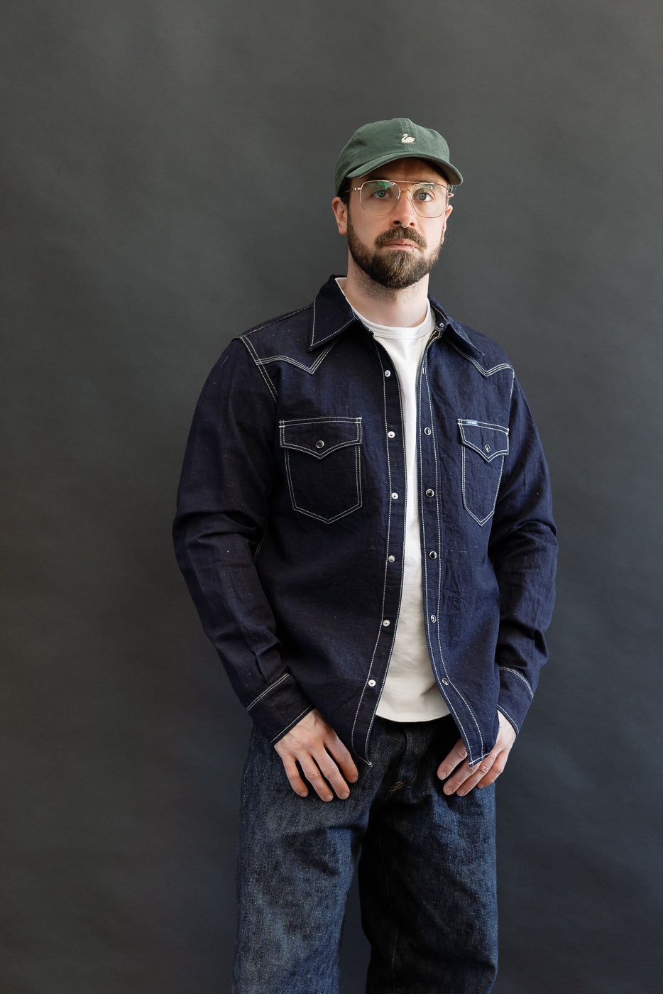 Man in IHSH-444-IND - 7oz Cotton Linen Chambray Western Shirt, featuring indigo chambray fabric, white stitching, snap fastenings, and western yokes, styled with jeans, showcasing premium menswear from Dant.