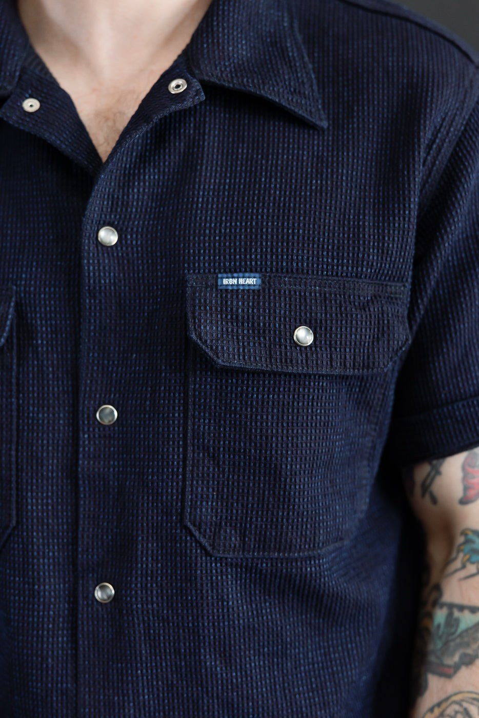 Close-up front view of male model wearing navy waffle knit short sleeve shirt with button chest pocket, collar, and Iron Heart tag.