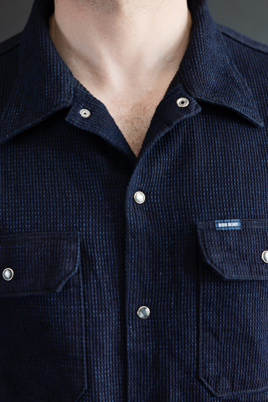 Close-up front view of male model wearing navy waffle-knit shirt with button collar, chest pockets, and 'IRON HEART' tag.