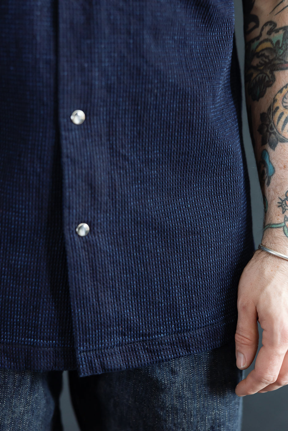 Close-up front view of navy blue textured shirt with silver buttons, worn by male model, 5'9