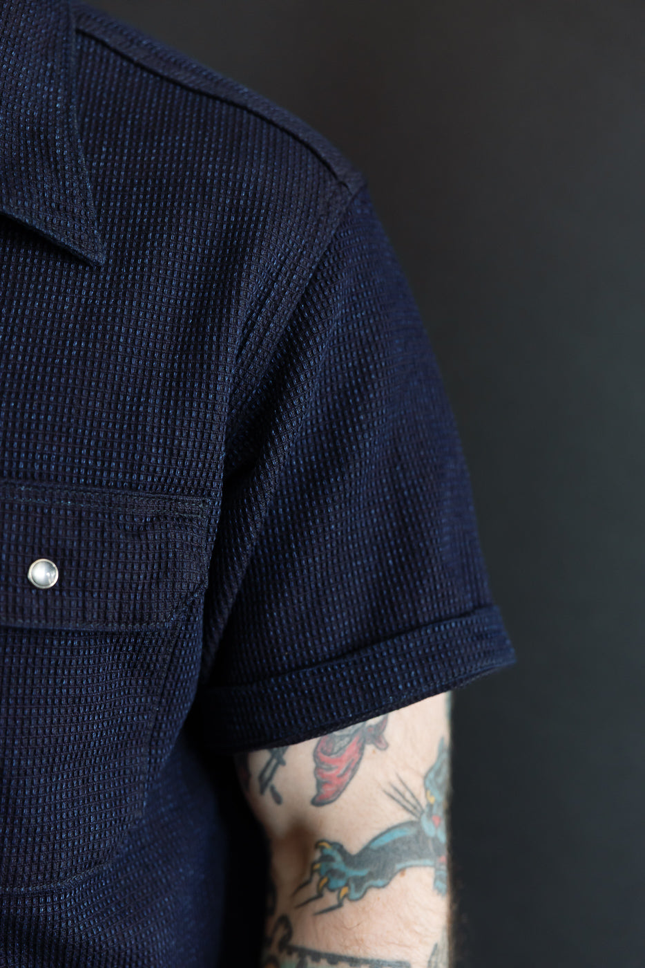 Close-up front view of navy waffle knit short-sleeve shirt on male model, showing collar, chest pocket with button, sleeve hem