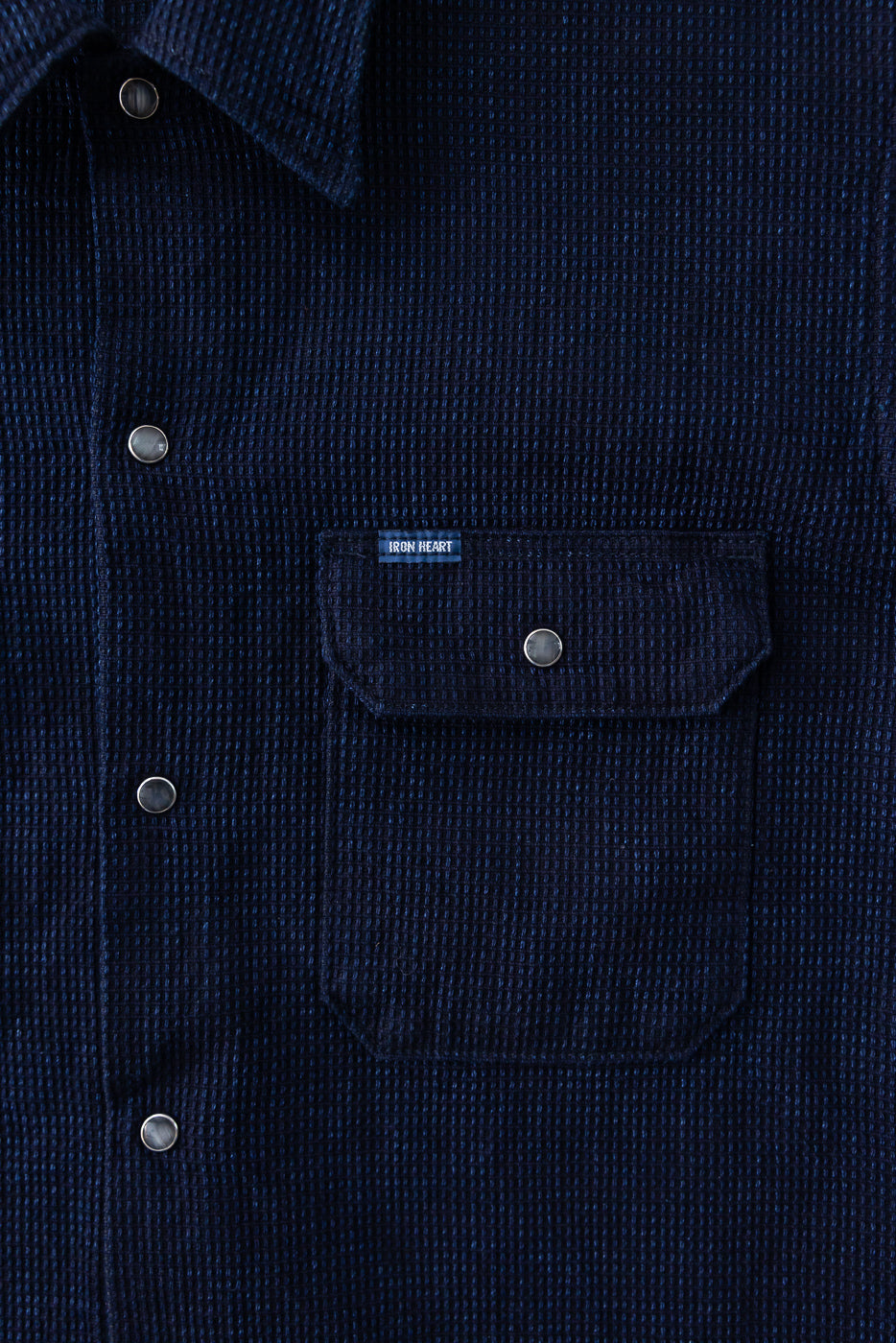 Close-up front view of navy waffle knit shirt with button chest pocket, 'IRON HEART' tag, and silver buttons
