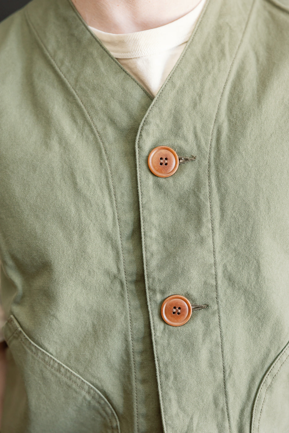 Close-up front of olive duck canvas hunting vest, wood buttons, male model, athletic build.