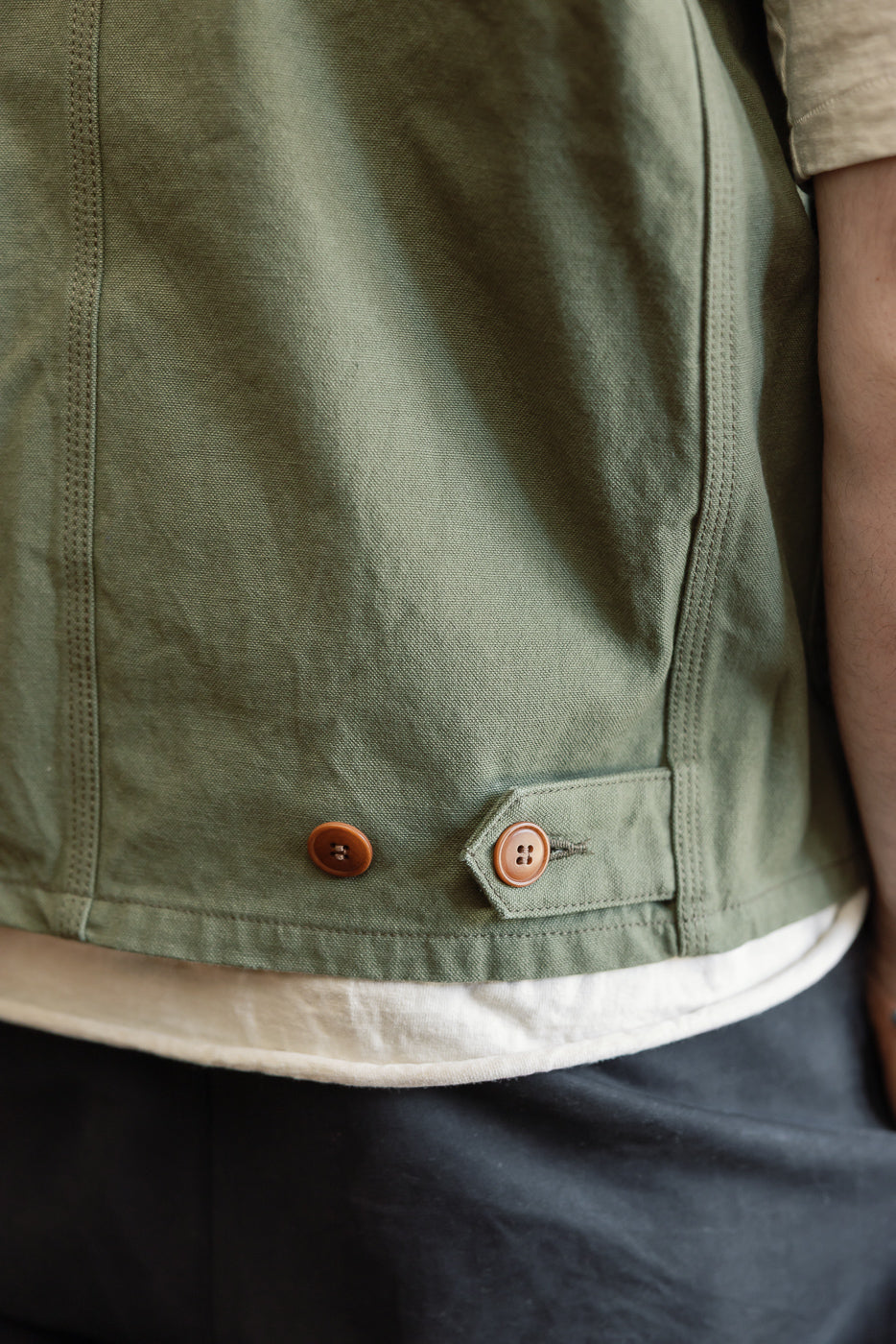 Close-up of rear hem and side buttons on olive duck canvas hunting vest, male model, athletic build