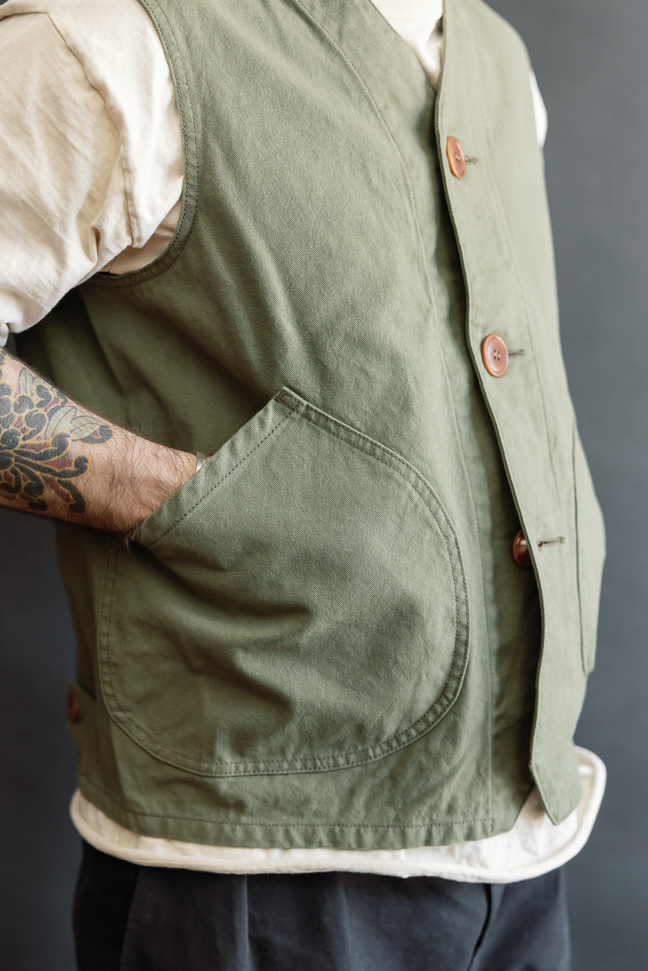 Close-up of olive green duck canvas hunting vest front side, worn by male model 5'9