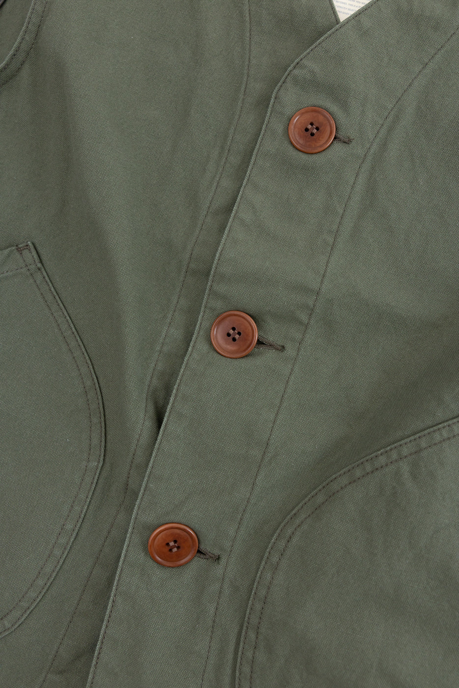 Close-up of olive duck canvas vest front, showing brown buttons and pocket stitching detail.