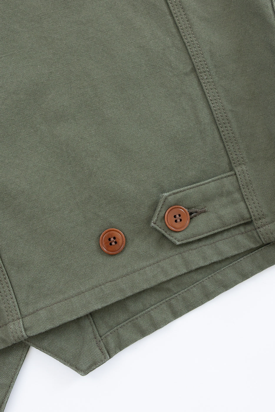 Close-up of olive duck canvas vest hem, showing front side with brown buttons and fabric texture.