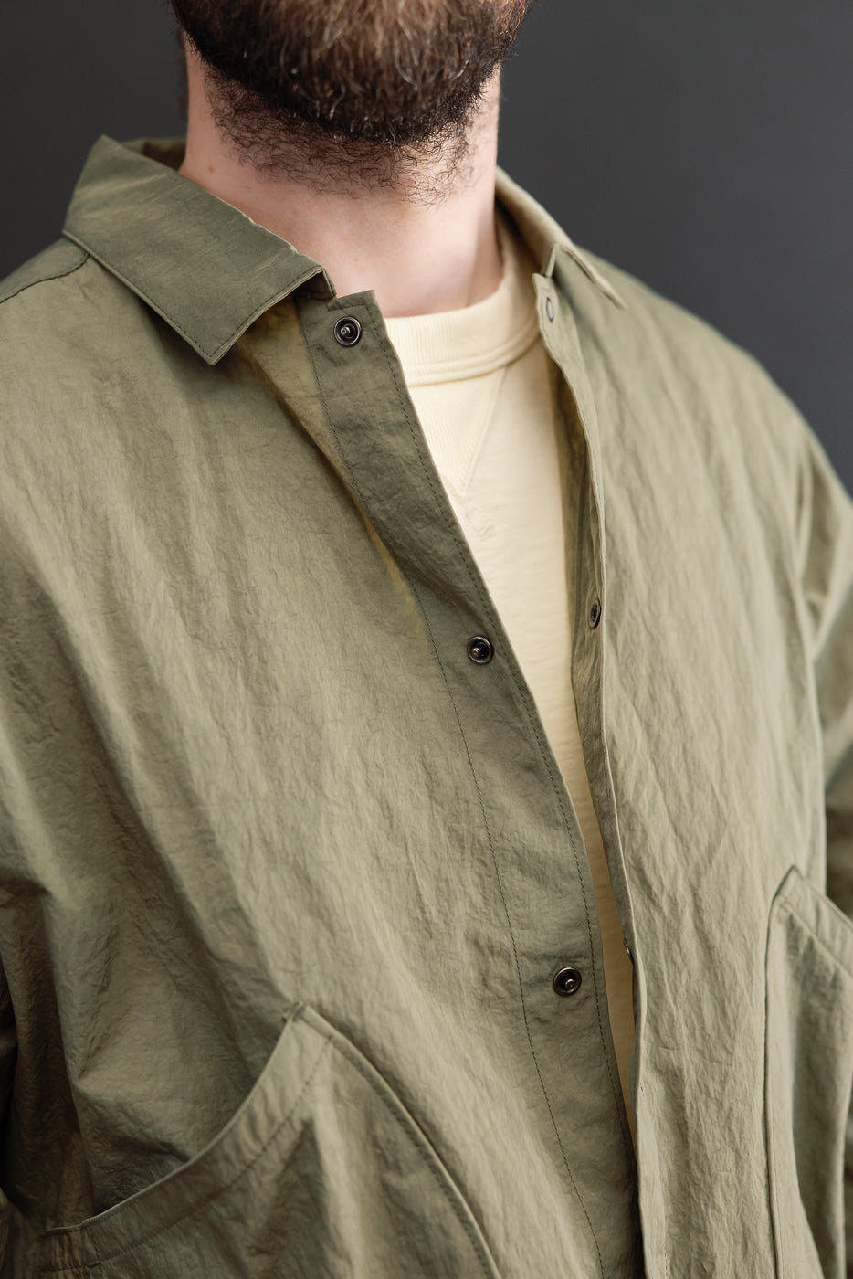Close-up front view of an olive green button-down shirt showing fabric texture and dark buttons.