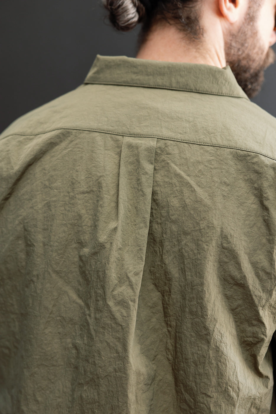 Close-up back view of an olive green linen shirt showing crinkled fabric texture.
