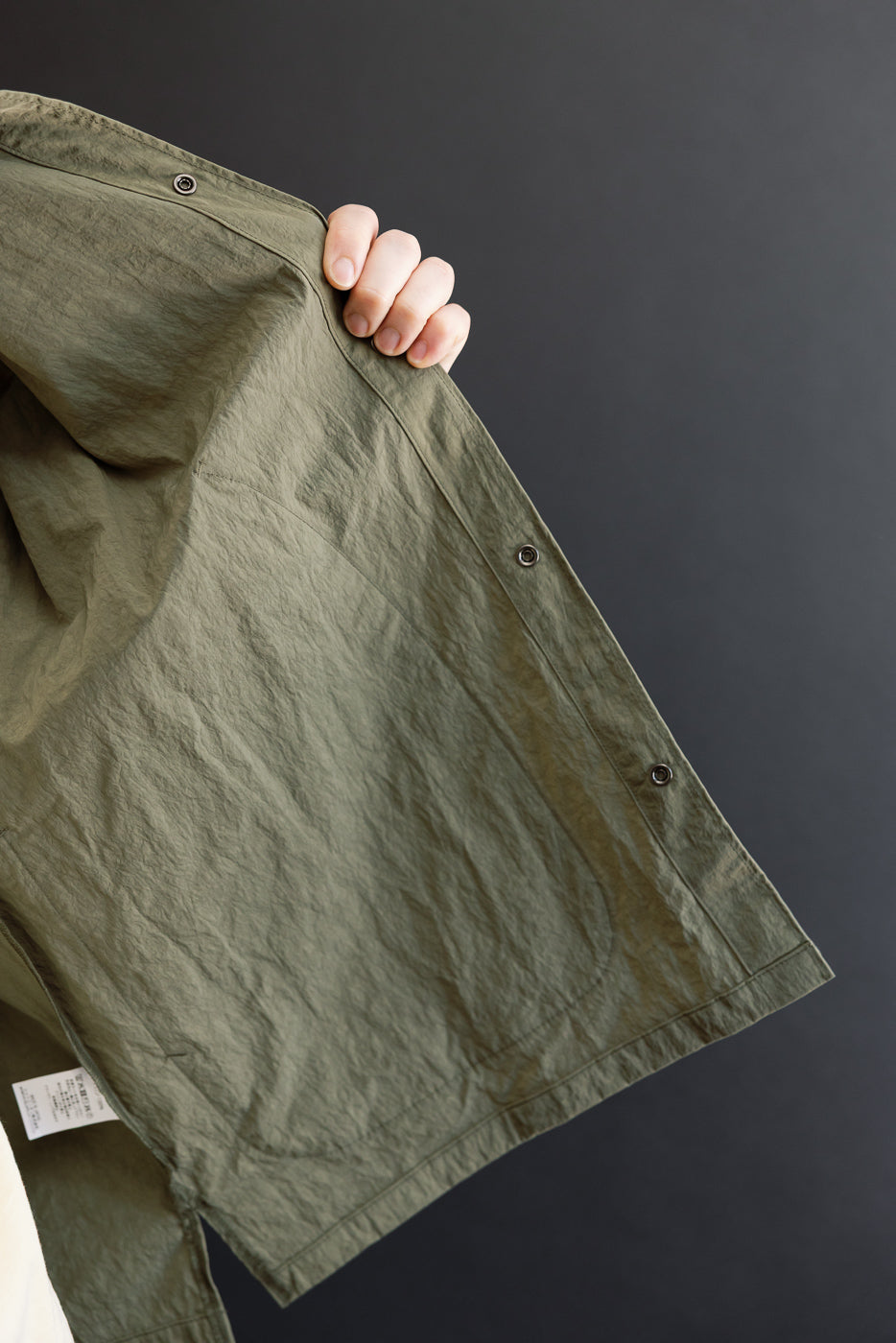 Close-up of the front side fabric texture and button detail on an olive green garment.