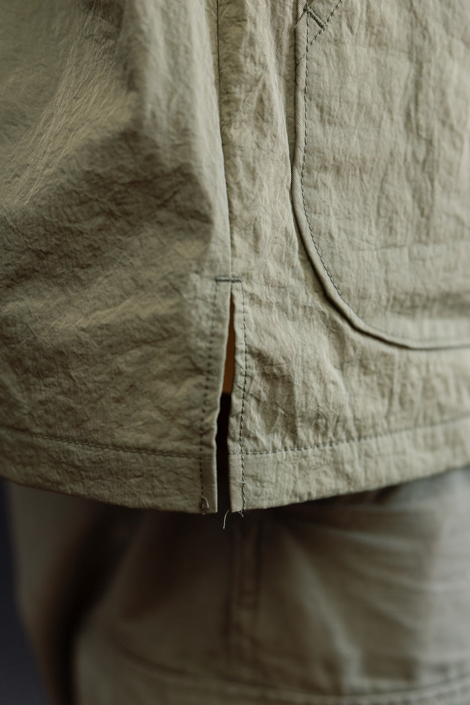 Close-up of the side hem and side slit of a crinkled olive green garment.