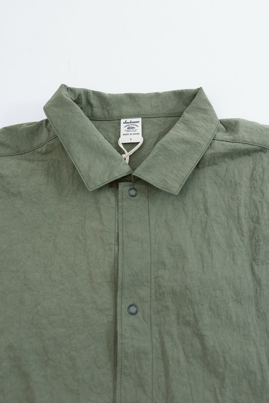 Close-up front view of olive green shirt collar and neckline showing fabric texture and tag.