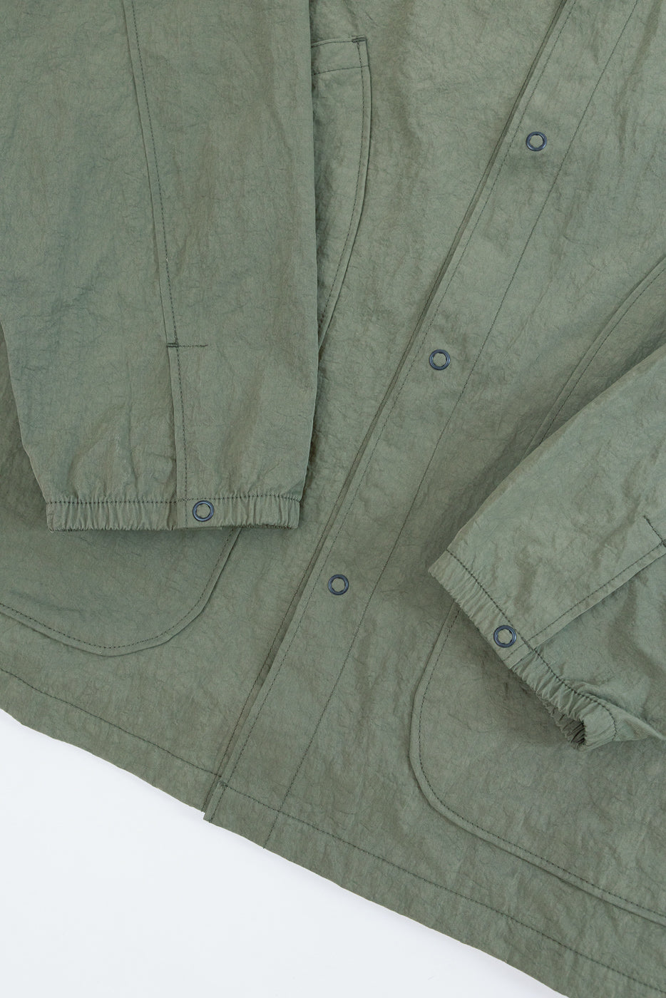 Close-up front view of a sage green jacket showing wrinkled fabric texture and snap buttons.