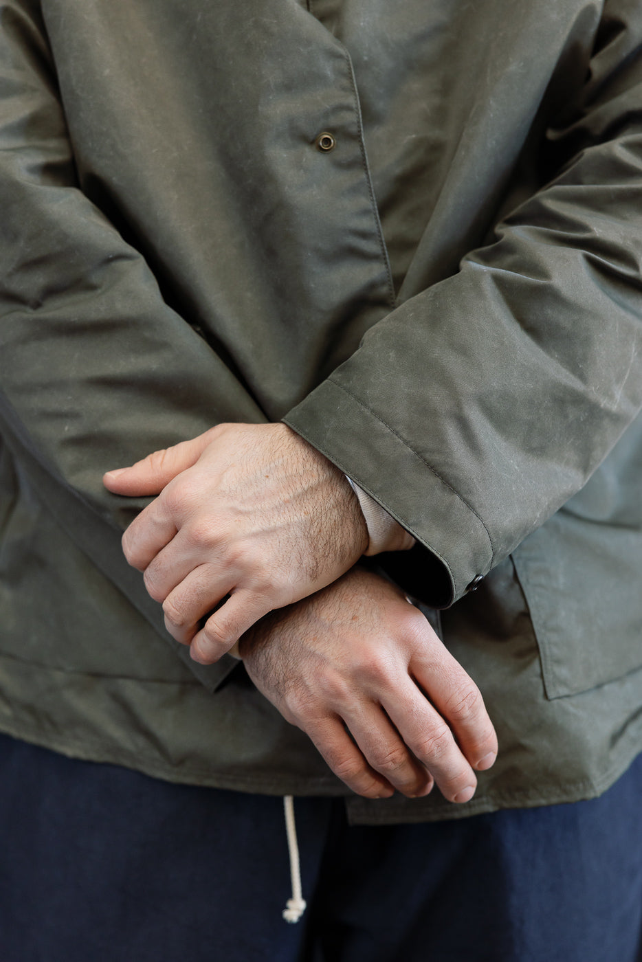 Close-up of front lower section of olive collarless jacket, showing snap button detail, worn by a male model 5'9