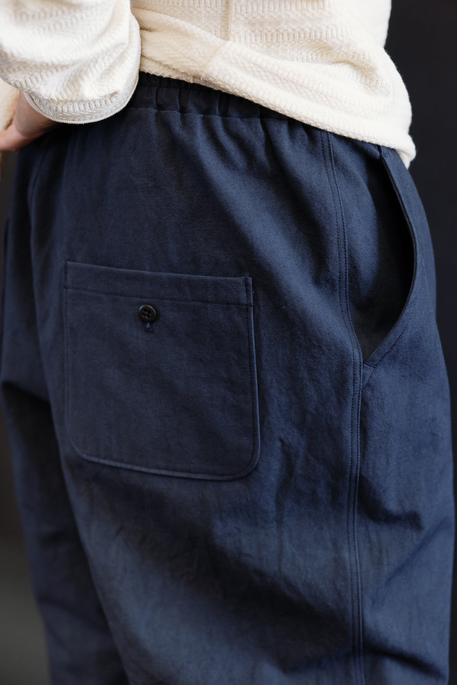 Close-up of men's navy canvas pants, back left side, showing buttoned patch pocket. Model is male, 5'9