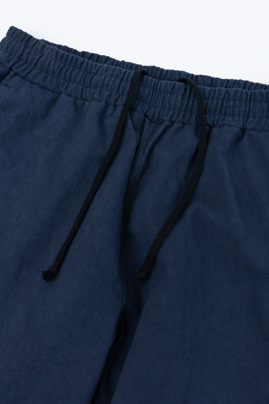 Close-up of front waist on navy canvas pants with elastic waistband and black drawstring.