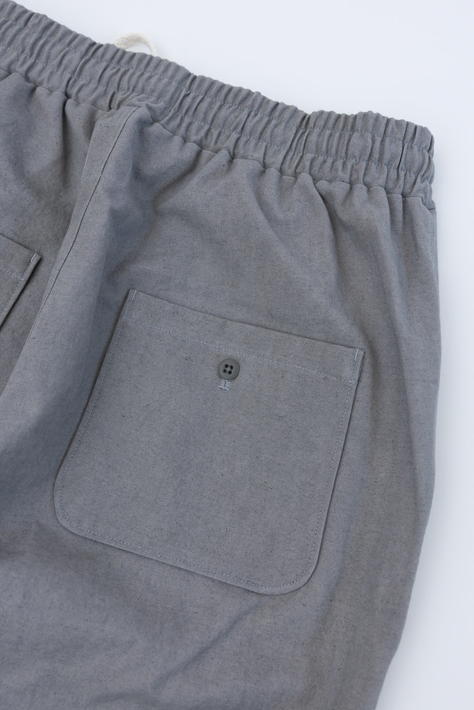 Close-up of back side of gray canvas pants showing elastic waistband and buttoned pocket