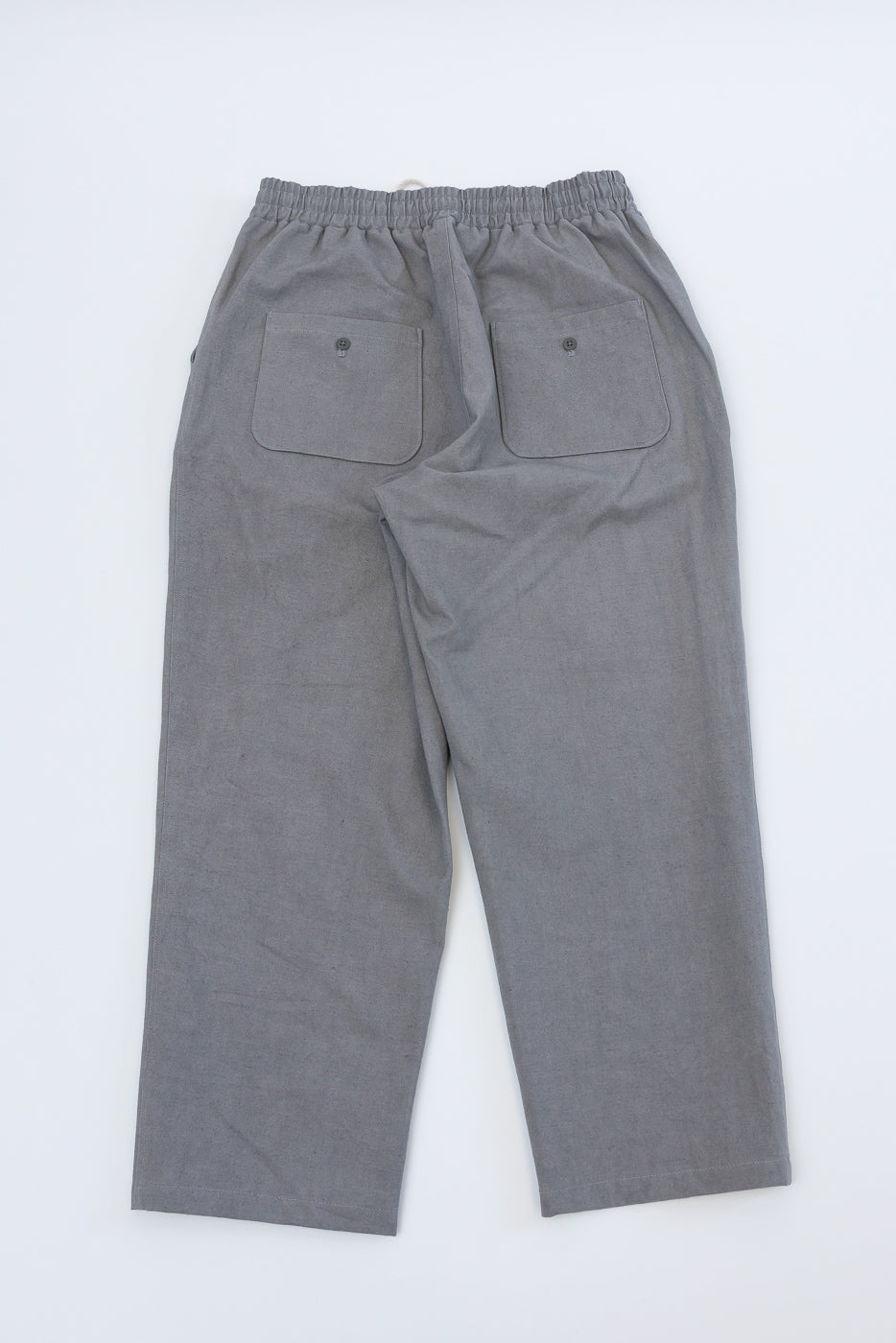 Flat lay of rookie canvas pants in solid gray, showing full back with elastic waist and two buttoned pockets.