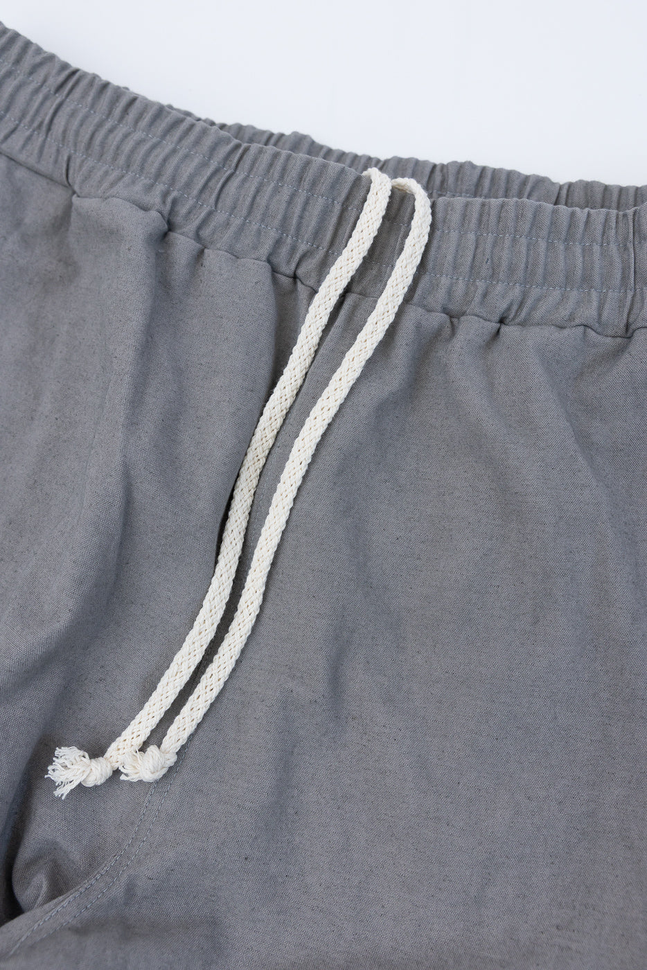 Close-up of the front waist area of gray canvas pants, showing drawstring and elastic waistband.
