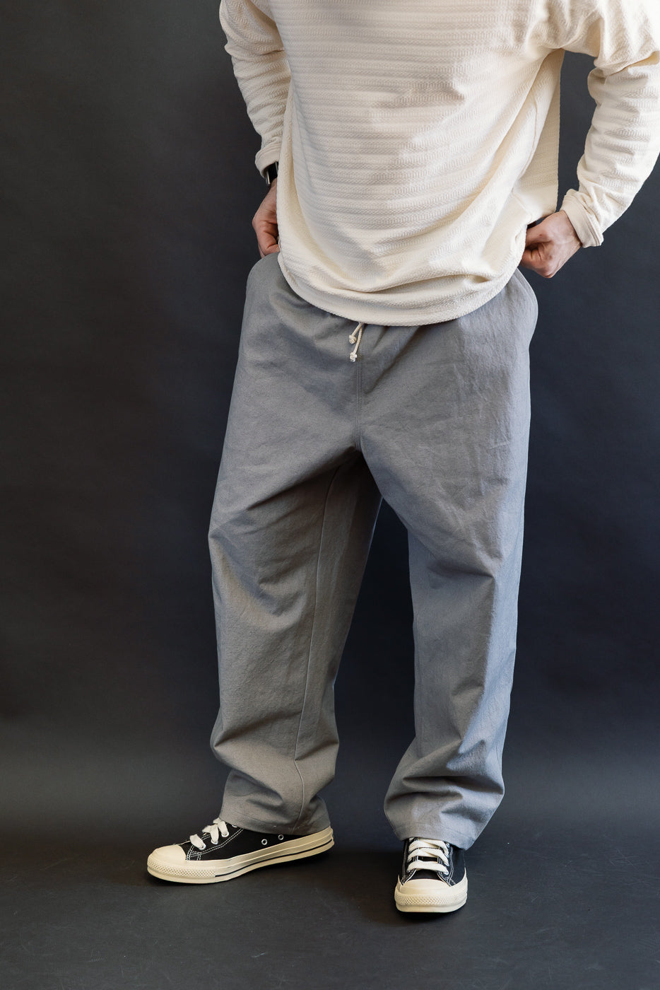 Front view, full-body of male model 5'9, 165lbs athletic build wearing gray canvas drawstring pants.