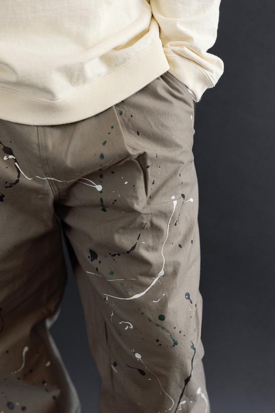 Close-up side view of tan paint-splattered trousers on a male model.