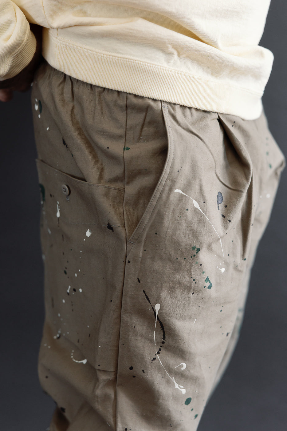 Side view close-up of tan paint-splattered trousers on a male model, 5'9