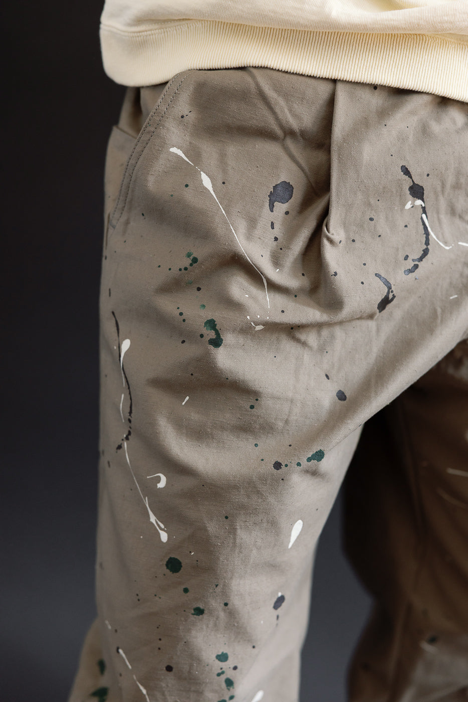Close-up of the front left side of paint-splattered tan trousers on a male model.