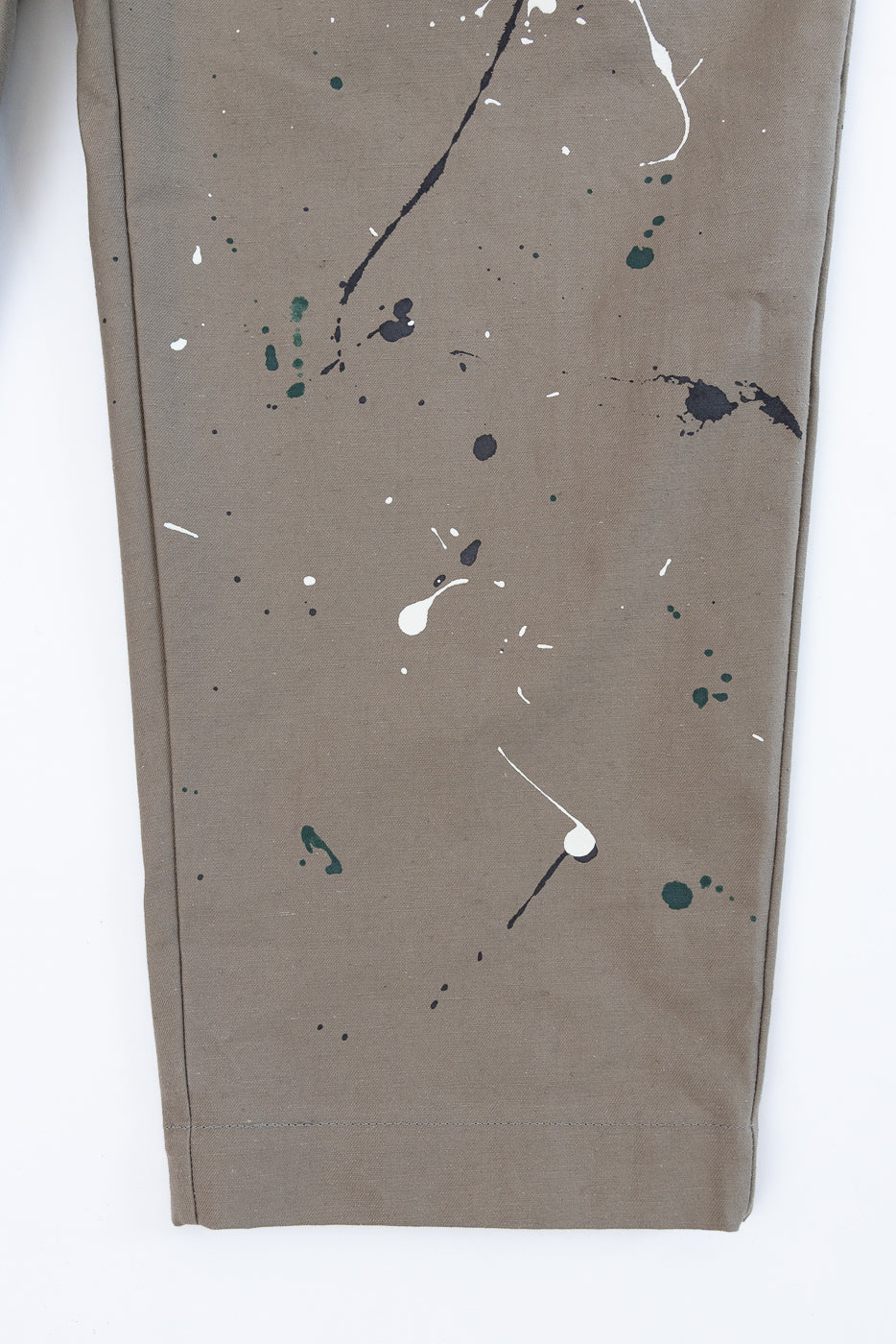 Close-up of the bottom leg and hem of olive green paint-splattered trousers.