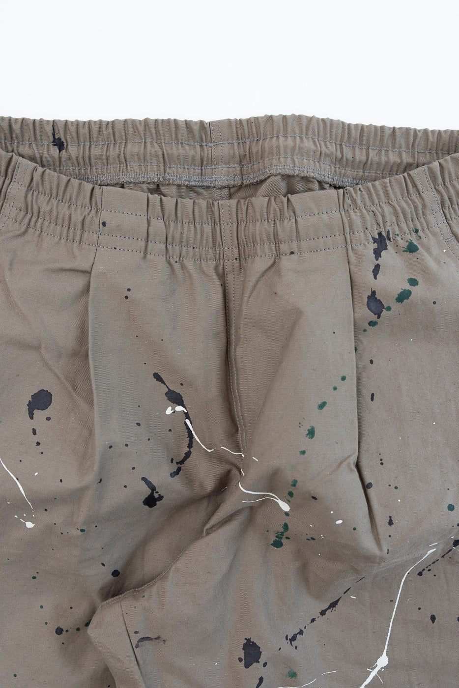 Close-up front view of the elastic waistband and paint splatter detail on tan trousers.