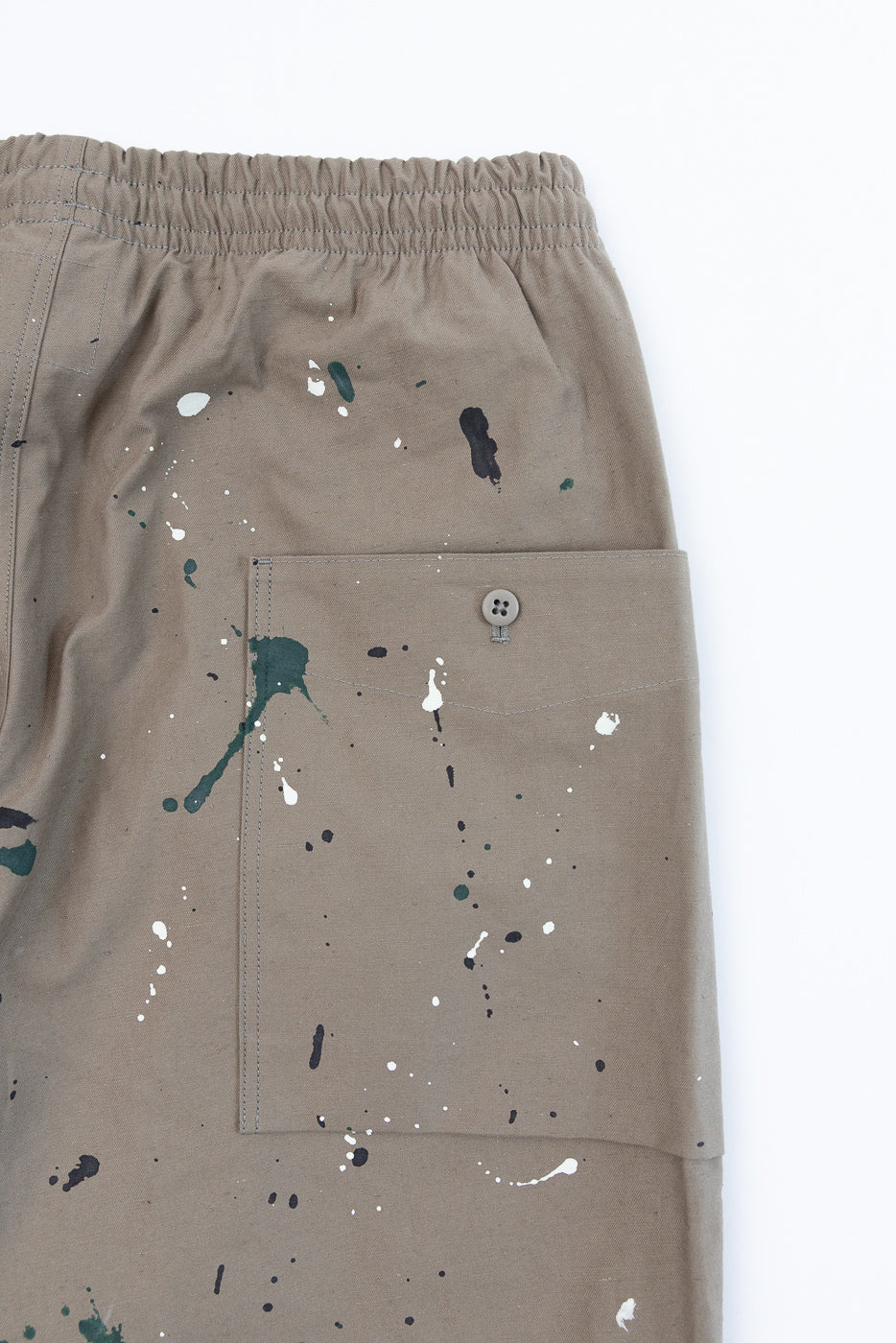 Flat lay front view of tan cargo shorts featuring paint splatter details and a side pocket.