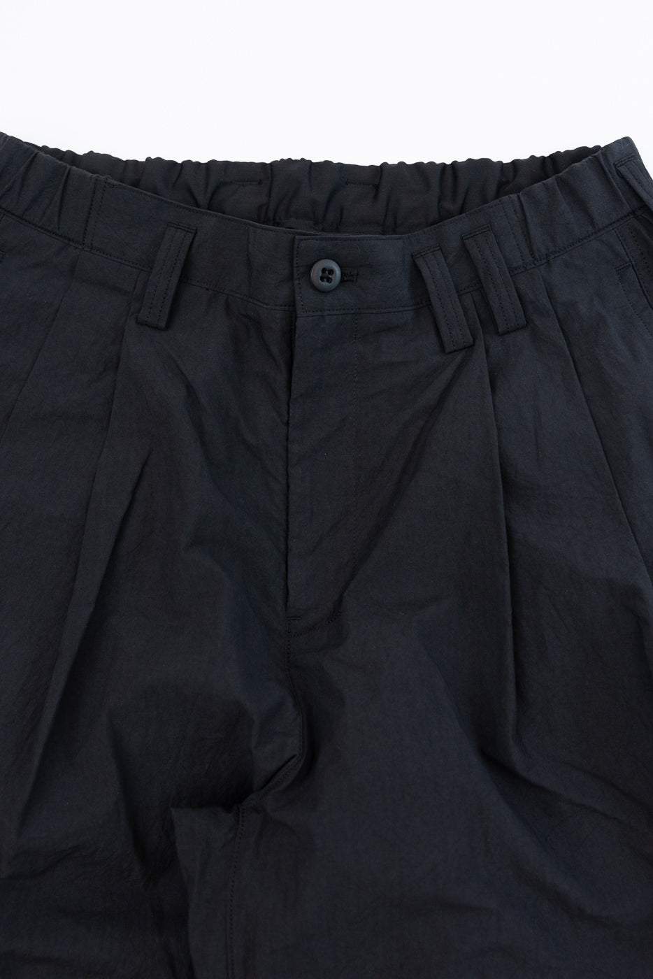 Close-up front view of black casual pants with elastic waist, button closure, and pleats