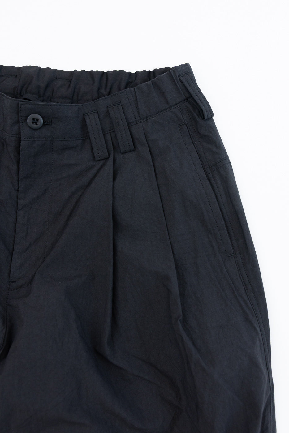 Close-up front view of black casual pants with elastic waist, button closure, and pleated front detail