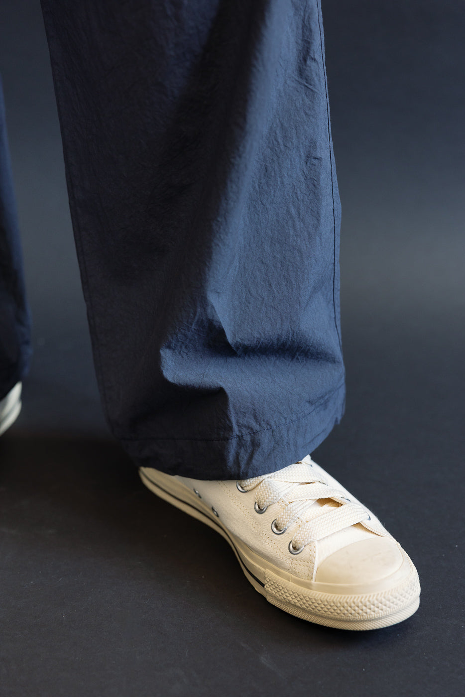 Close-up of navy wide-leg pants hem with cream canvas sneaker, male model 5'9