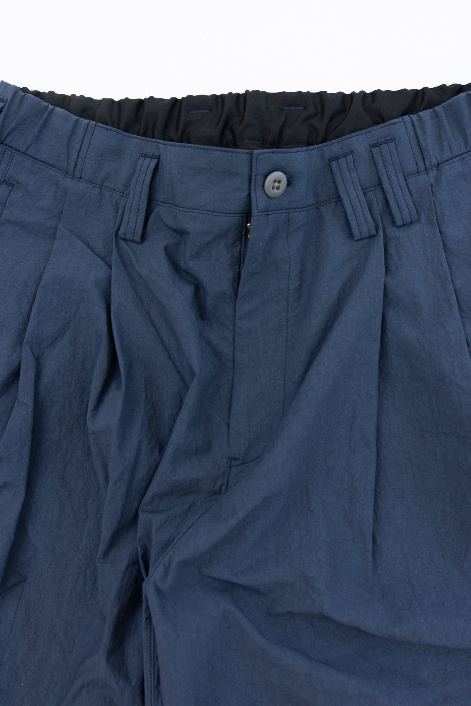 Close-up front view of navy blue casual pants with button closure, pleats, and elastic waistband